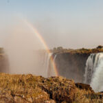 A vibrant rainbow arcs over the mist of Victoria Falls.