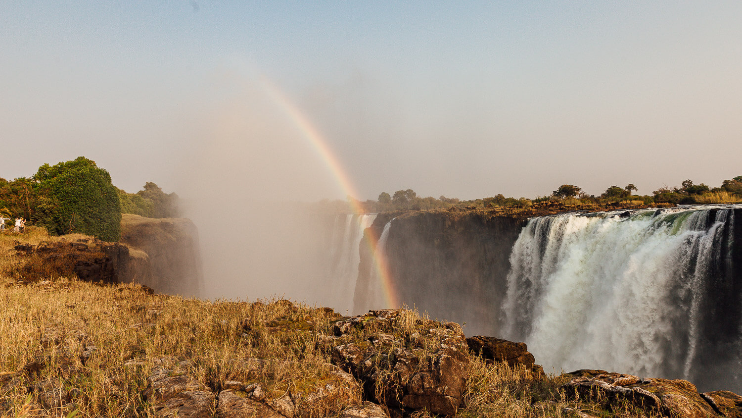 A vibrant rainbow arcs over the mist of Victoria Falls.